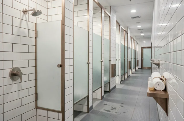 Rangée de cabines de douche modernes dans une salle de sport Basic Fit avec carrelage blanc et parois en verre dépoli